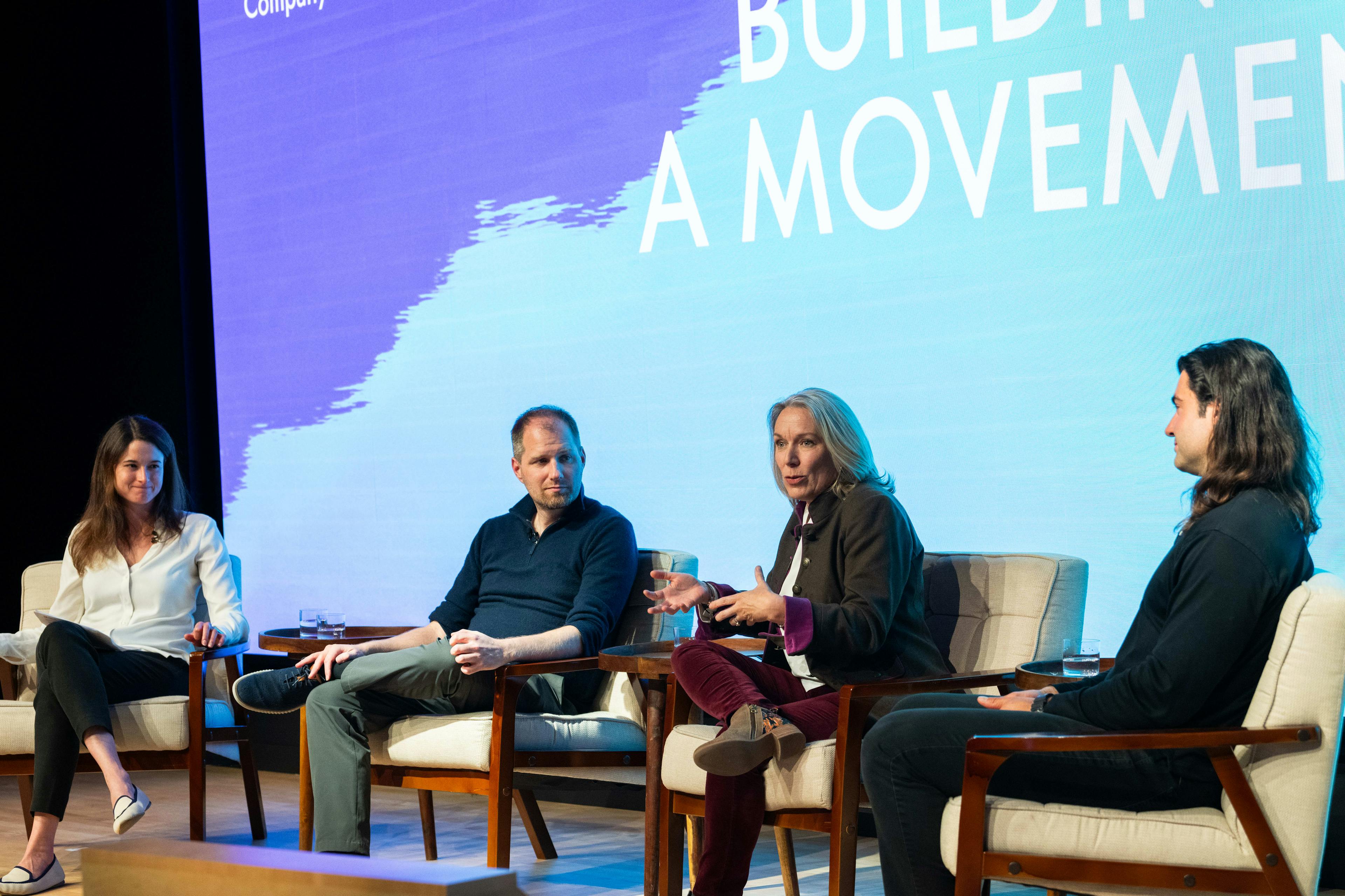 A panel of four people sitting on a stage, with "Building a movement" written in the background