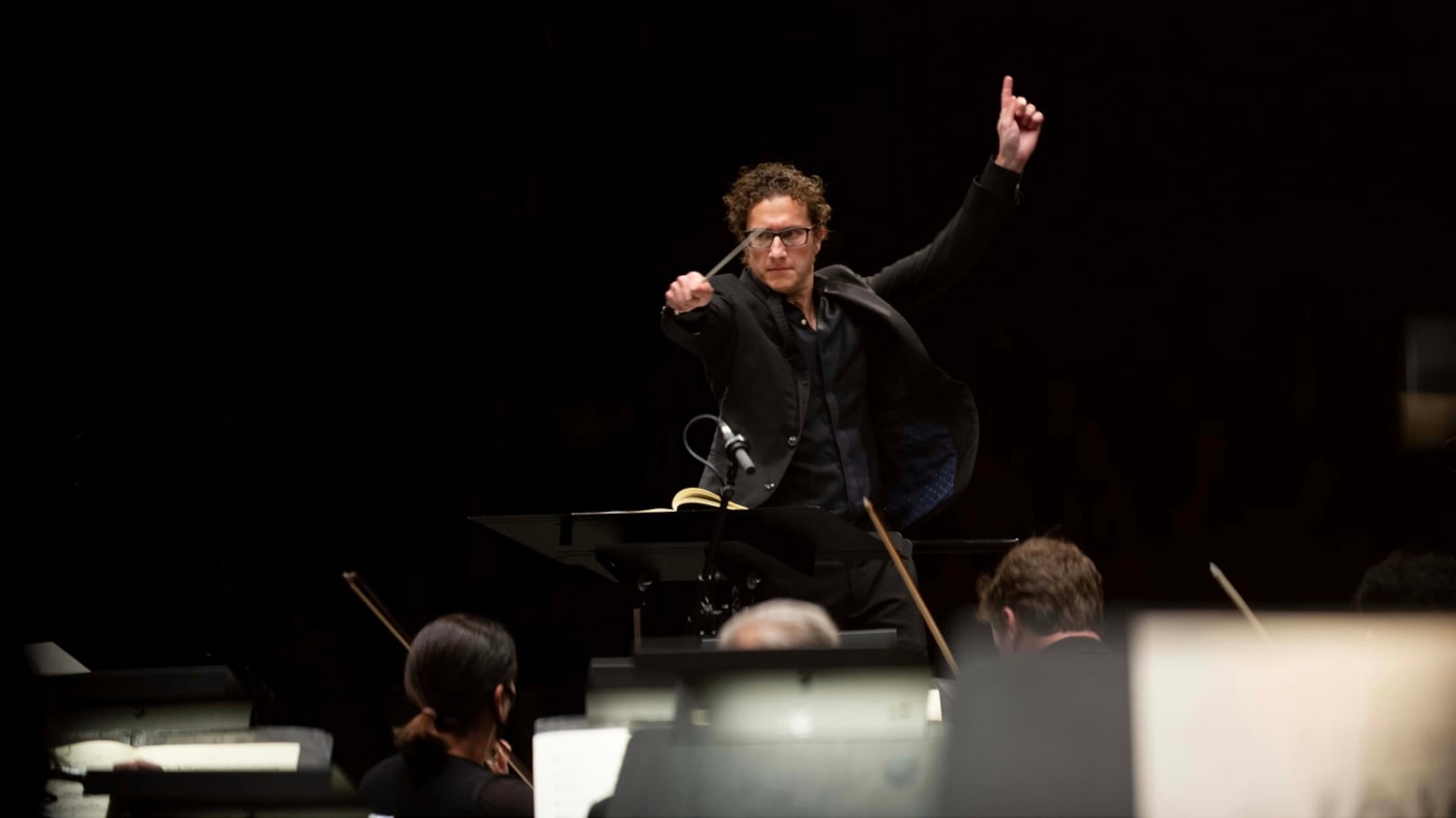 A conductor stands with arms in motion before the orchestra